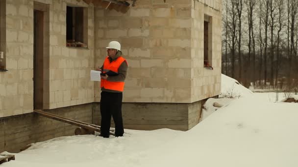 Inspektor bezpieczeństwa pracownika rozmawia przez telefon, w pobliżu nowego budynku — Wideo stockowe