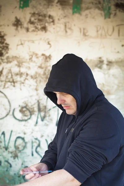 Drogensüchtiger Mann mit Spritze in der Hand vor Wandhintergrund — Stockfoto