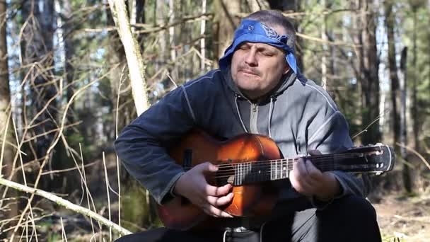 Man sitter på en stubbe och spelar gitarr i skogen — Stockvideo