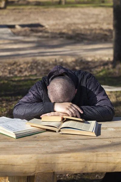 Student lying asleep on books outside on a bench