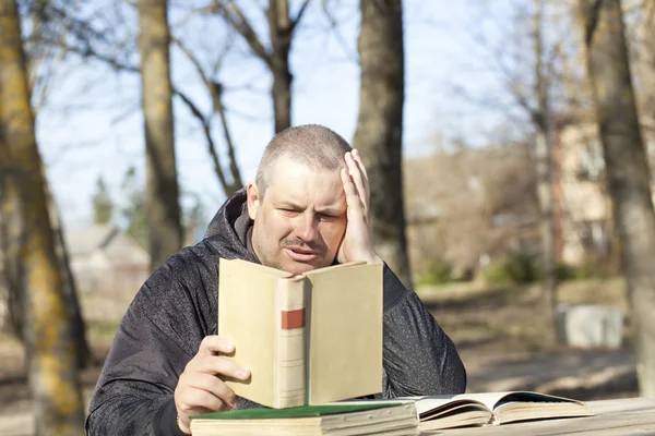 Man die leest een boek buitenshuis op een bankje in het park — Stockfoto