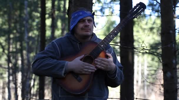Spelen gitaar in het bos leunend tegen boom aflevering een man — Stockvideo