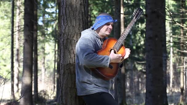 Чоловік грає на гітарі в лісі, спираючись на дерево епізод два — стокове відео