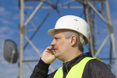 Engineer talking on the cell phone near to gsm tower clipart