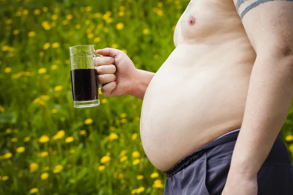 Hombre gordo con una cerveza en la mano sobre fondo de campo de diente de león — Foto de Stock