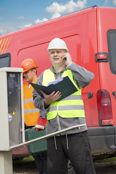 Electricians with cell phone and folder near switchboard — Stock Photo, Image