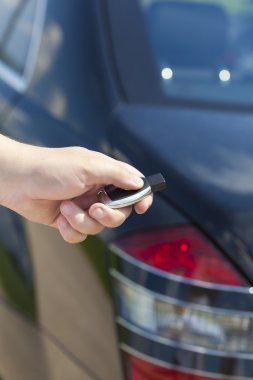 Hand with a car alarm remote control at the back of the car clipart