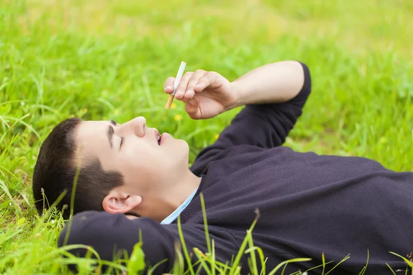 Boy with a cigarette lying in a meadow — Stock Photo, Image