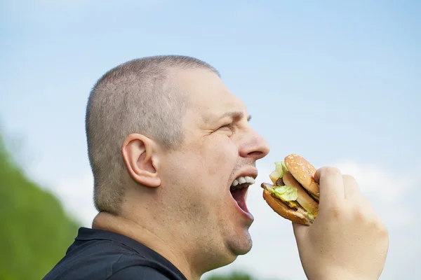 Homem começando comer hambúrguer em um fundo céu azul — Fotografia de Stock