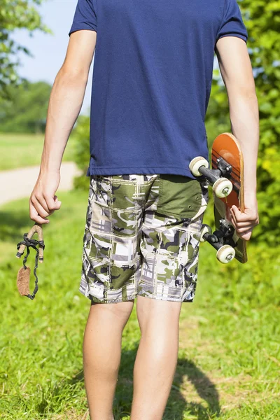 Ragazzo con fionda e skateboard su strada rurale — Foto Stock