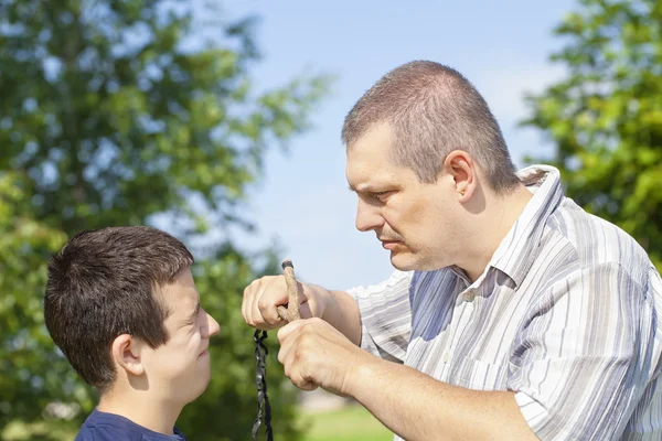 Angry man with slingshot in hand against the boy — Stock Photo, Image