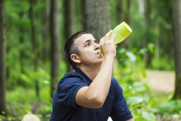 Niño beber agua cerca de trotar sendero en el bosque — Foto de Stock