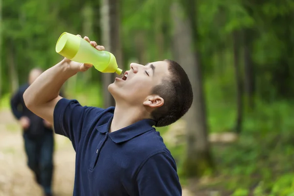 Αγόρι πόσιμο νερό για τζόκινγκ μονοπάτι μέσα στο δάσος — Φωτογραφία Αρχείου