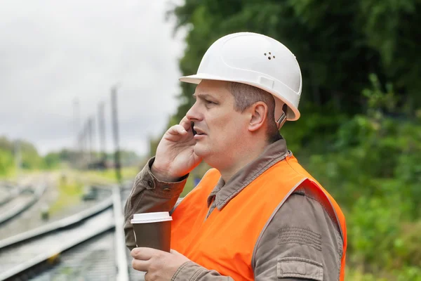 Pracownik z kawy i telefon komórkowy na linii kolejowej — Zdjęcie stockowe