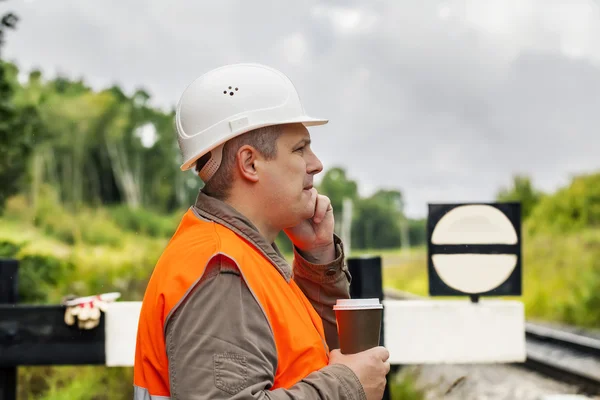 Werknemer met een koffie en mobiele telefoon op de spoorlijn in de zomer — Stockfoto