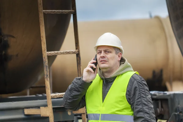 Spoorweg werknemer met mobiele telefoon in de buurt van tankwagons — Stockfoto