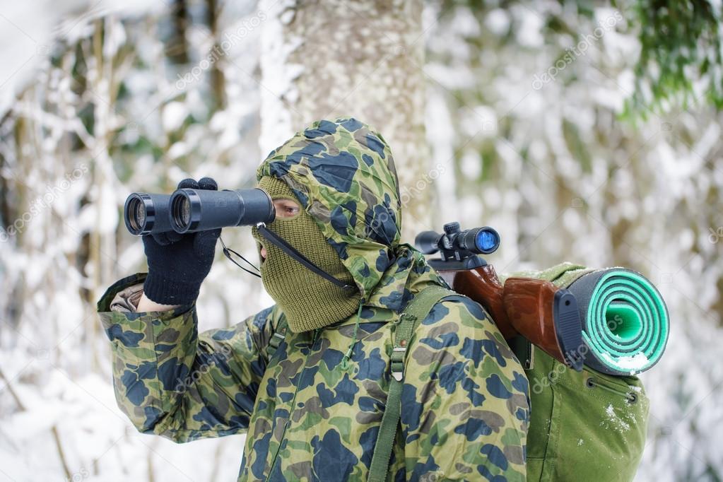 Hunter with binoculars and optical rifle in woods