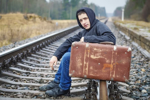 Teenage boy with a suitcase on the railway in rain — Stock Photo, Image