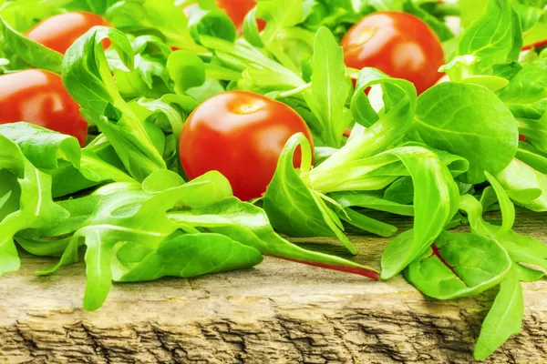 Lettuce leaves with tomatoes on a wooden table — Stock Photo, Image