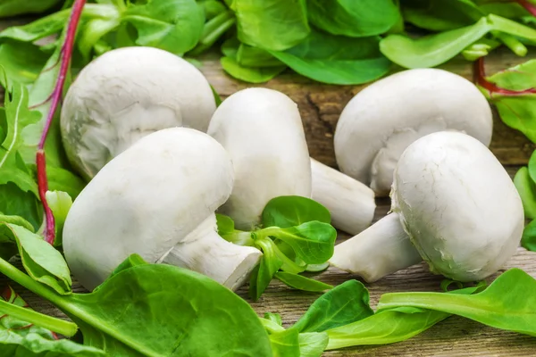 Champiñones frescos con hojas de lechuga sobre una mesa de madera — Foto de Stock