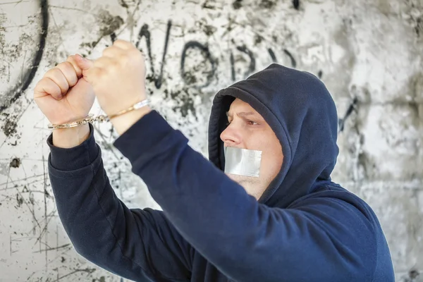 Hostage in handcuffs with tape on the mouth near wall — Stock Photo, Image
