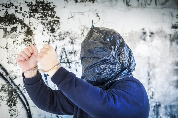 Hostage in handcuffs and with a bag on head near wall — Stock Photo, Image