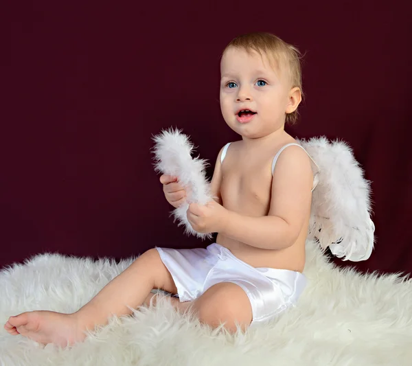 Criança vestida como um anjo sentado em um fundo vermelho — Fotografia de Stock