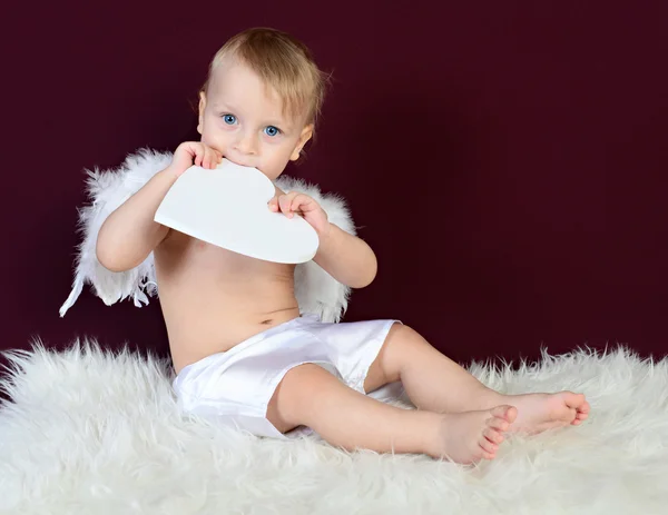 Kid dressed as an angel sitting on a red background — Stock Photo, Image