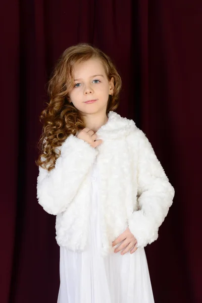 Hermosa chica en vestido blanco y un abrigo de piel sobre un fondo rojo — Foto de Stock