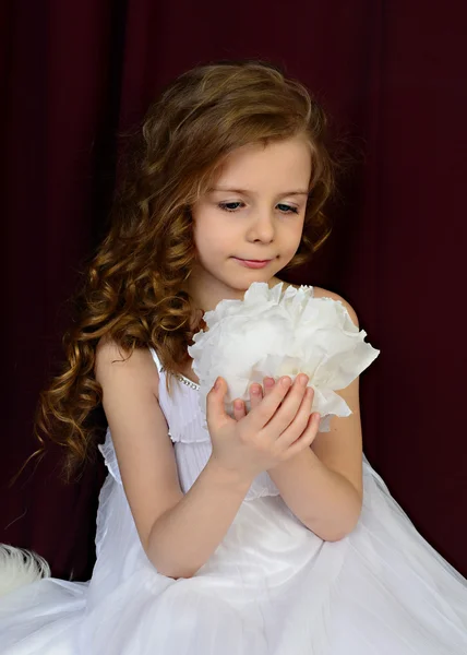 Flickan i en vacker vit klänning med en vit papper blomma på en röd bakgrund — Stockfoto