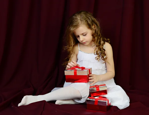 Piękna dziewczyna siedzi na czerwonym tle z darów — Zdjęcie stockowe