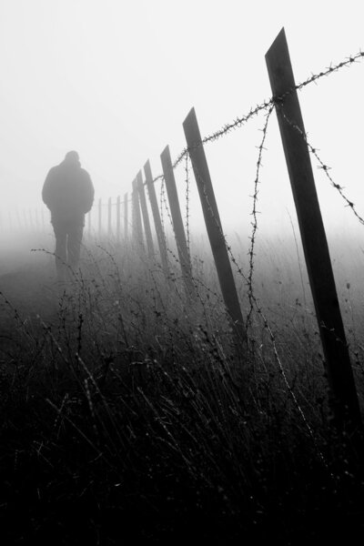 Man walking near barbed wire fence in dense fog