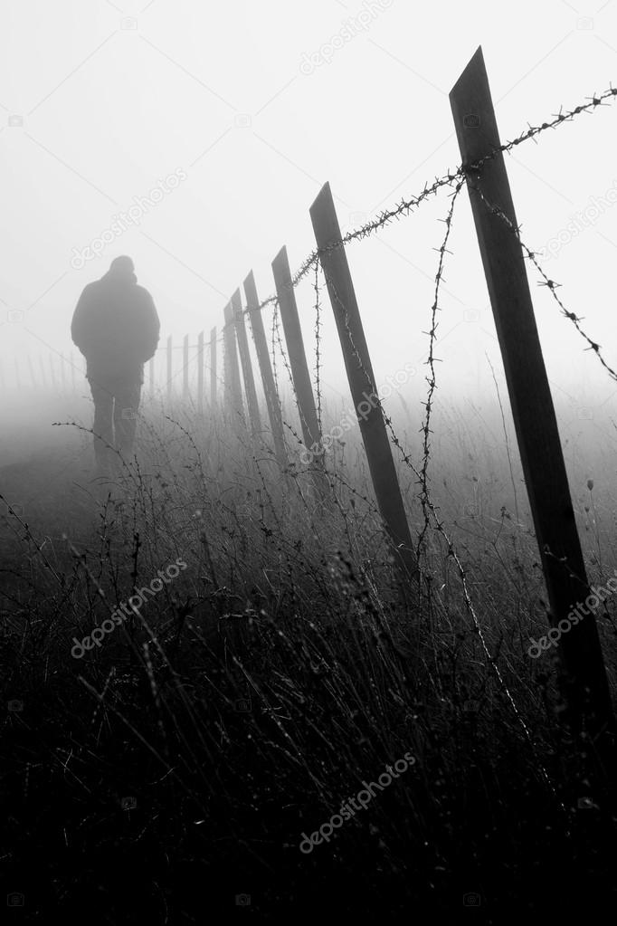 Man walking near barbed wire fence in dense fog