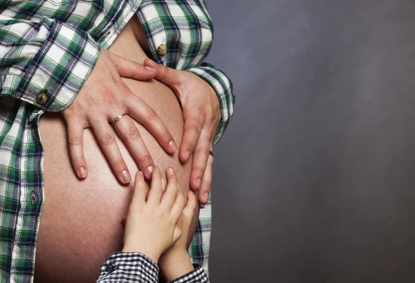 Mains de l'enfant sur le ventre de la femme enceinte — Photo