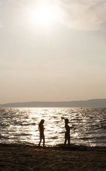 Two kids silhouettes playing on beach at sunset — Stock Photo, Image