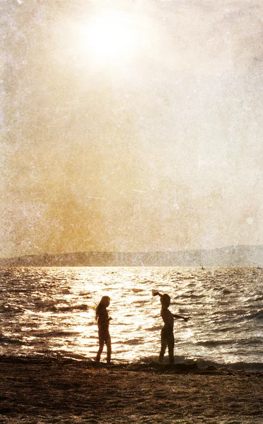 Dwa dzieci sylwetki gra na plaży o zachodzie słońca — Zdjęcie stockowe