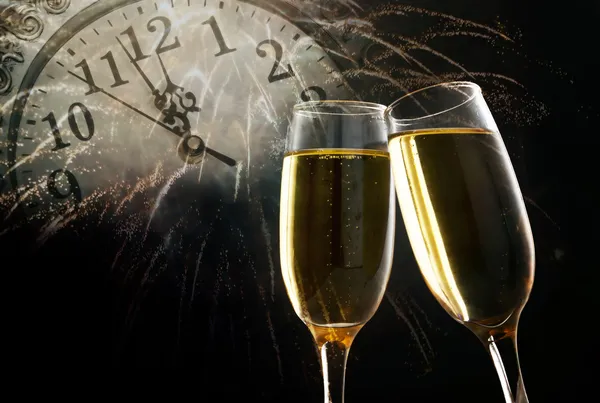 Glasses with champagne against fireworks and clock close to midnight — Stock Photo, Image