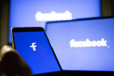 CLUJ-NAPOCA, ROMANIA - Ekim 2021: Bir kişi Facebook rrom akıllı telefonu ve bilgisayarına giriş yapıyor.