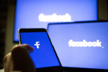 CLUJ-NAPOCA, ROMANIA - Ekim 2021: Bir kişi Facebook rrom akıllı telefonu ve bilgisayarına giriş yapıyor.