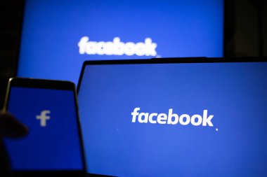CLUJ-NAPOCA, ROMANIA - Ekim 2021: Bir kişi Facebook rrom akıllı telefonu ve bilgisayarına giriş yapıyor.
