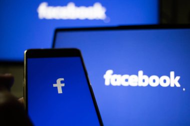 CLUJ-NAPOCA, ROMANIA - Ekim 2021: Bir kişi Facebook rrom akıllı telefonu ve bilgisayarına giriş yapıyor.