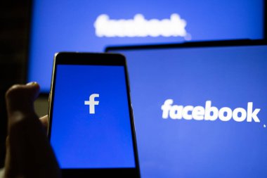CLUJ-NAPOCA, ROMANIA - Ekim 2021: Bir kişi Facebook rrom akıllı telefonu ve bilgisayarına giriş yapıyor.