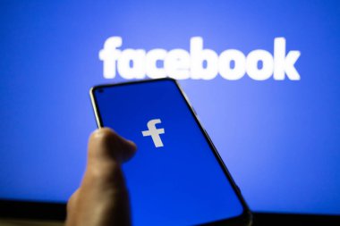 CLUJ-NAPOCA, ROMANIA - Ekim 2021: Bir kişi Facebook rrom akıllı telefonu ve bilgisayarına giriş yapıyor.