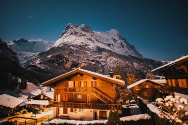Kış gecesi Grindelwald karlı dağı, yıldızlar ve ahşap ev