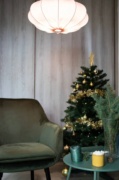 dark green room at Christmas with tree  chair  marshmallow drink in yellow mug on table