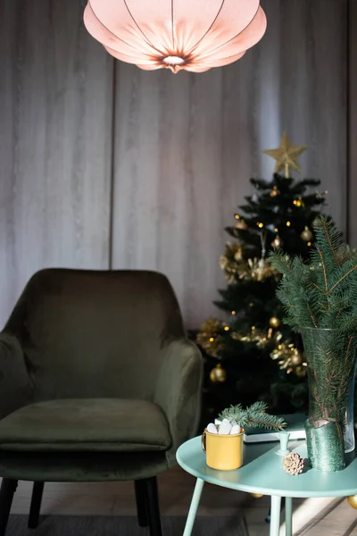 Koyu yeşil oda Noel 'de, ağaç sandalyeli marshmallow masasında sarı bardakta içecek. 