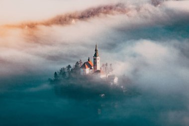 Sisli bir sabahta, Bled Blejsko Jezero Gölü 'nün muhteşem manzarası. Küçük bir adada Maria' nın Hacı Kilisesi ve arka planda Kanlı Kale ve Julian Alps.