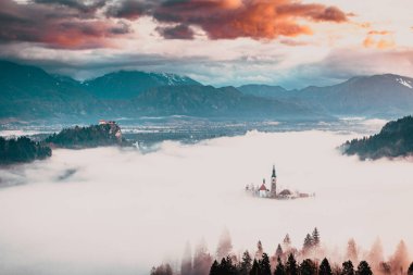 Sisli bir sabahta, Bled Blejsko Jezero Gölü 'nün muhteşem manzarası. Küçük bir adada Maria' nın Hacı Kilisesi ve arka planda Kanlı Kale ve Julian Alps.