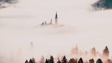 Sisli bir sabahta, Bled Blejsko Jezero Gölü 'nün muhteşem manzarası. Küçük bir adada Maria' nın Hacı Kilisesi ve arka planda Kanlı Kale ve Julian Alps.
