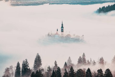 Sisli bir sabahta, Bled Blejsko Jezero Gölü 'nün muhteşem manzarası. Küçük bir adada Maria' nın Hacı Kilisesi ve arka planda Kanlı Kale ve Julian Alps.